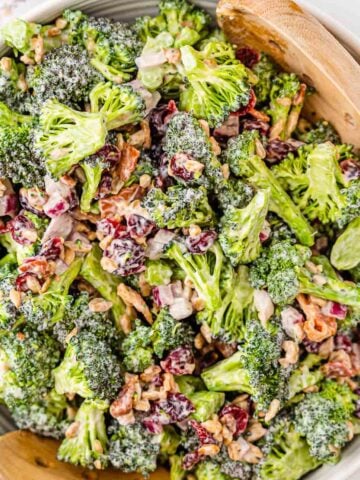 White bowl of broccoli salad with two wooden spoons.