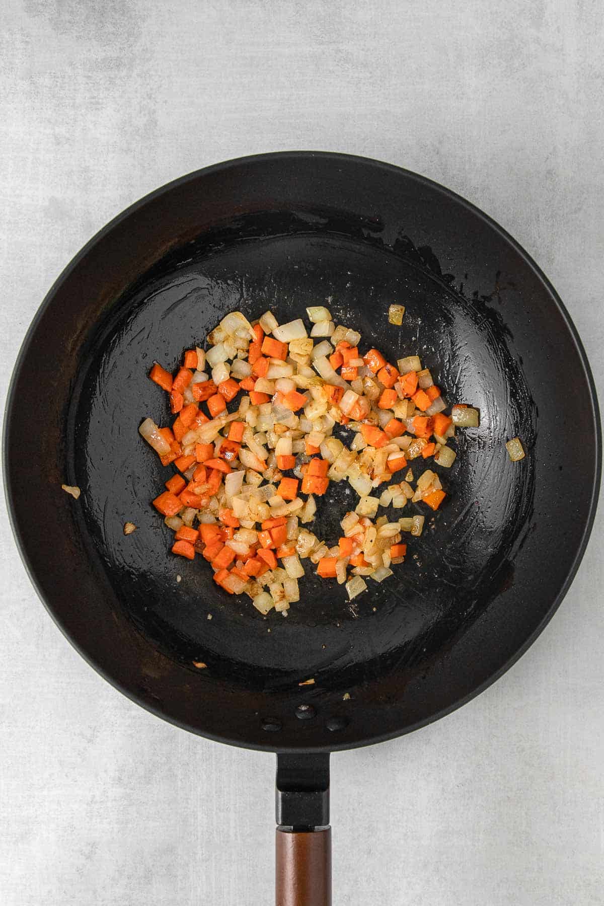 Large black skillet with diced onion and carrot cooking.
