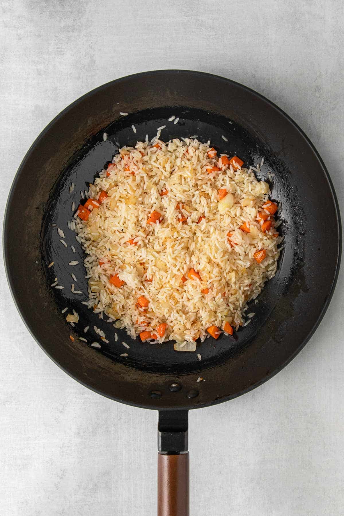 Large black skillet with rice and diced carrots cooking.