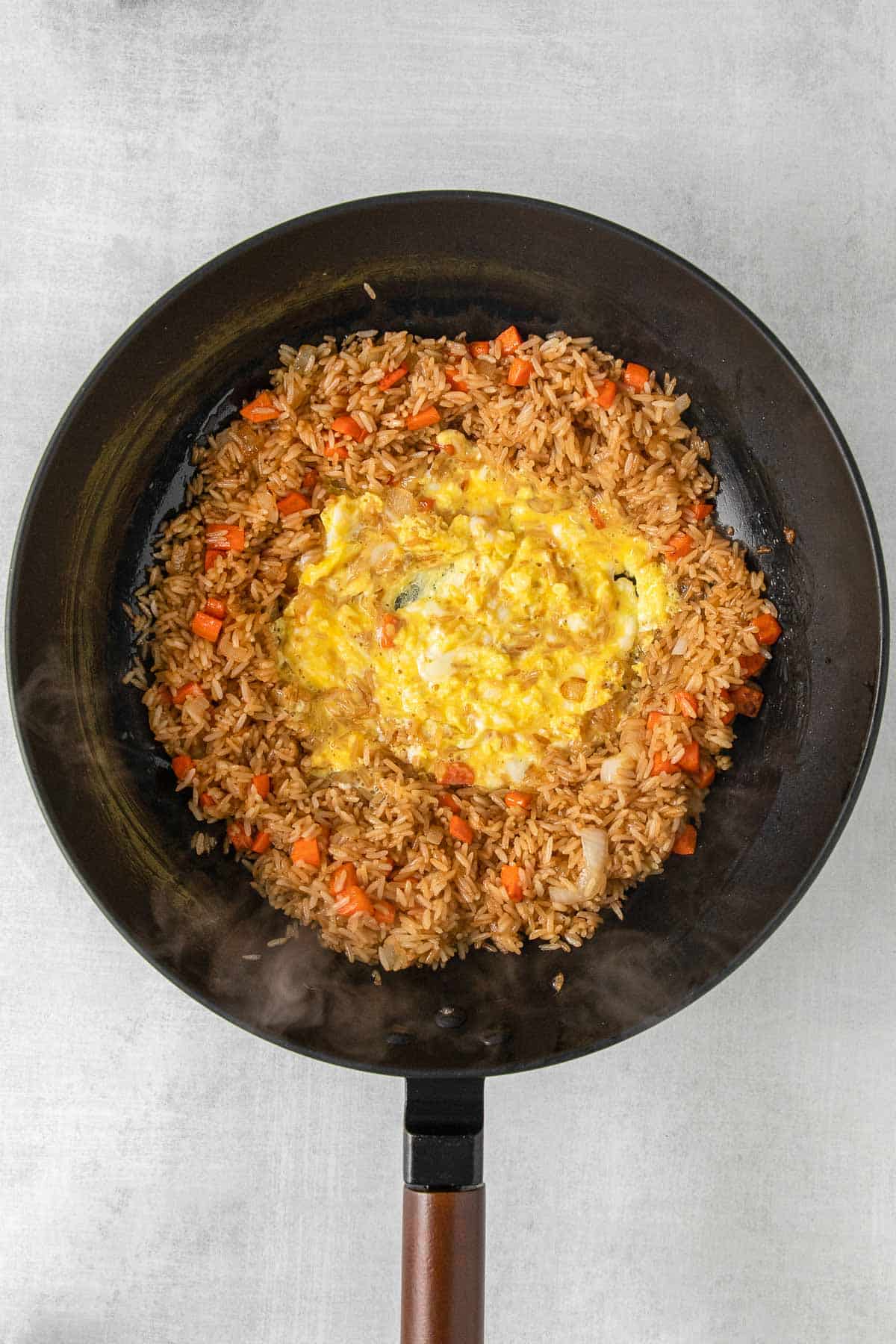 Large black skillet with beaten egg added to center of rice mixture.