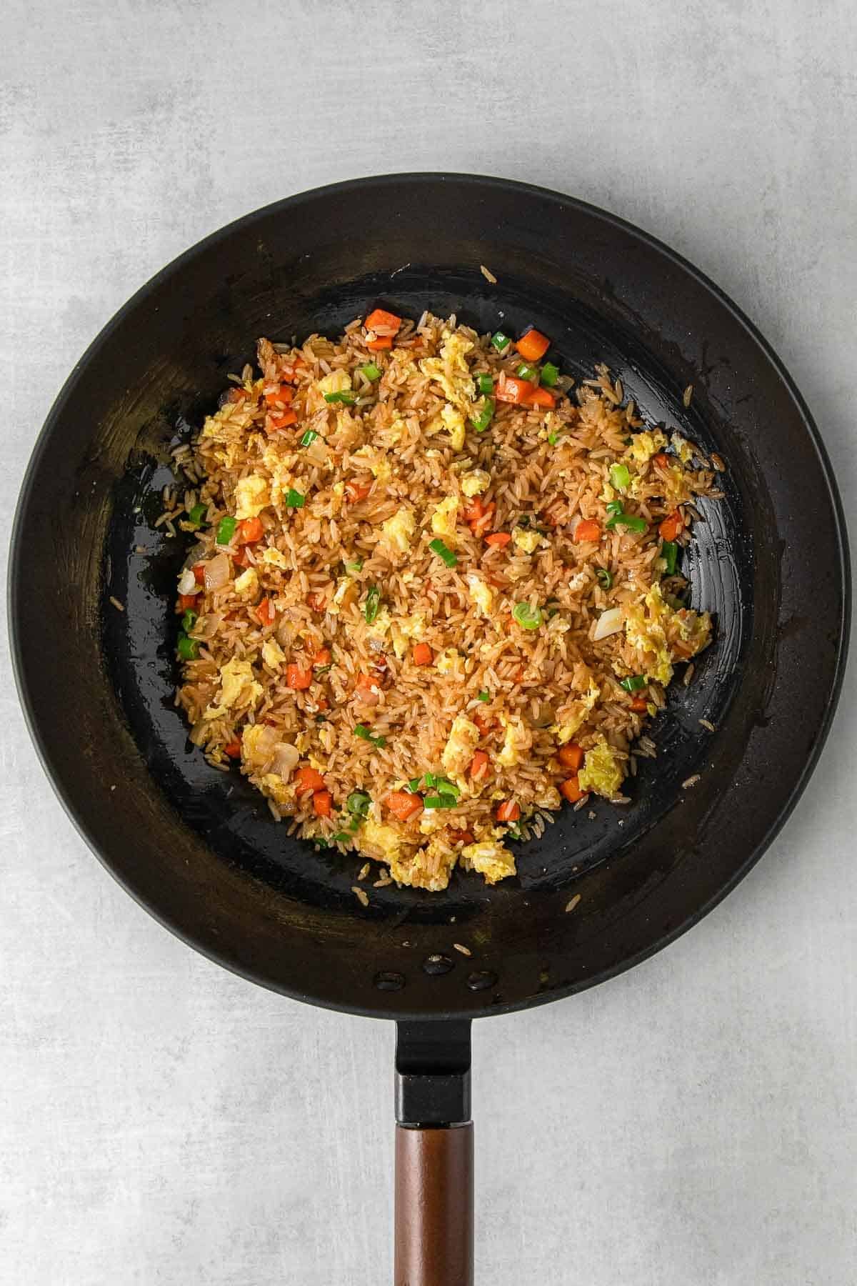 Cooked egg fried rice in large skillet with green onion garnish.