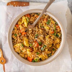 White bowl full of Egg Fried Rice with fork inserted.