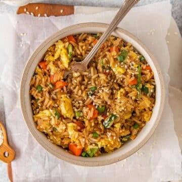 White bowl full of Egg Fried Rice with fork inserted.