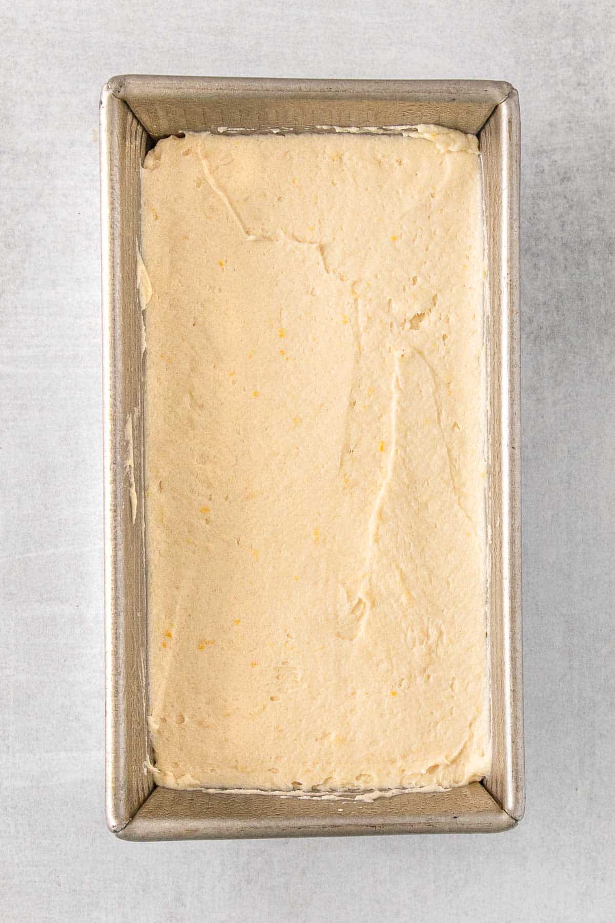 Metal loaf pan with lemon pound cake batter spread in.