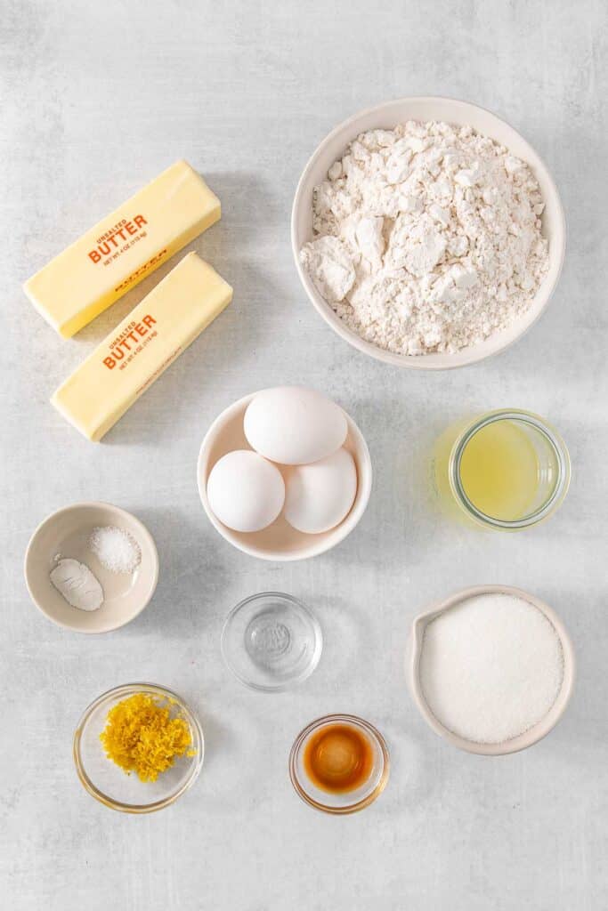 Several bowls of ingredients for Lemon Pound Cake - Butter, sugar, lemon, eggs, vanilla extract, lemon extract, flour, salt and baking powder.