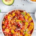 White bowl full of fresh mango salsa topped with cilantro and red onion.