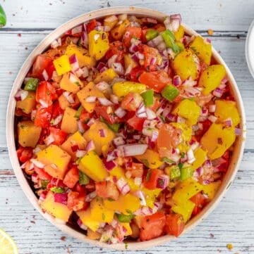 White bowl full of fresh mango salsa topped with cilantro and red onion.