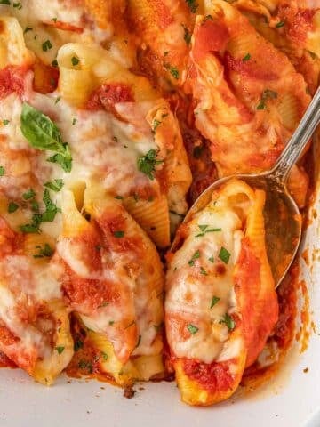 Close up of silver spoon scooping stuffed shell out of a white baking dish.