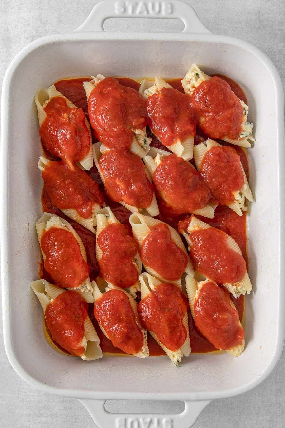 Stuffed shells in large baking dish with sauce drizzled overtop.