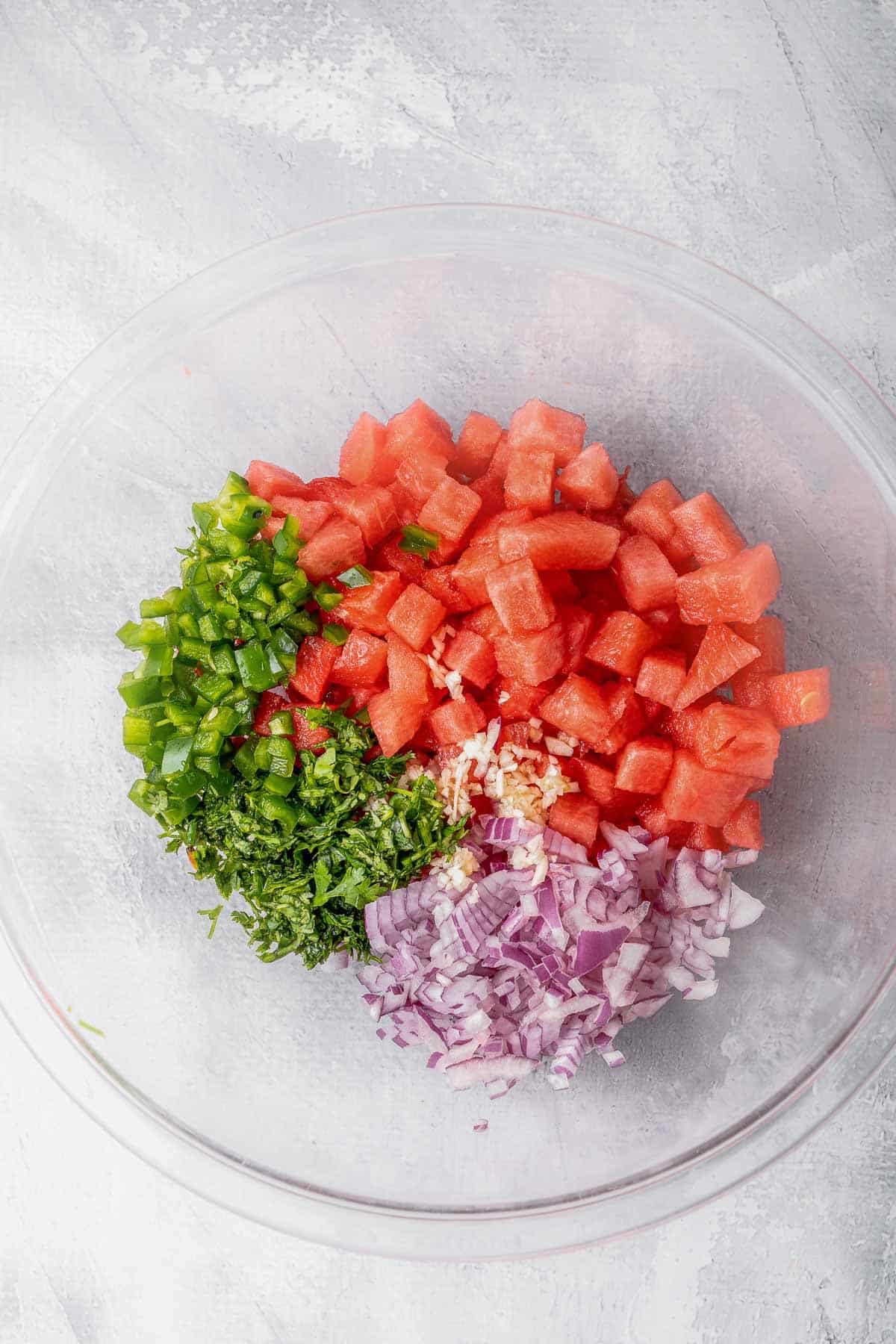 Large glass bowl of ingredients for Watermelon Salsa - watermelon, red onion, jalapeño, cilantro, garlic, lime juice, salt.