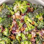 White bowl of broccoli salad with two wooden spoons.