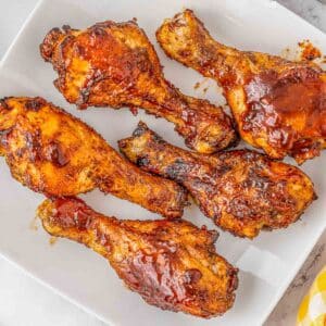 Multiple BBQ chicken drumsticks on a white plate.