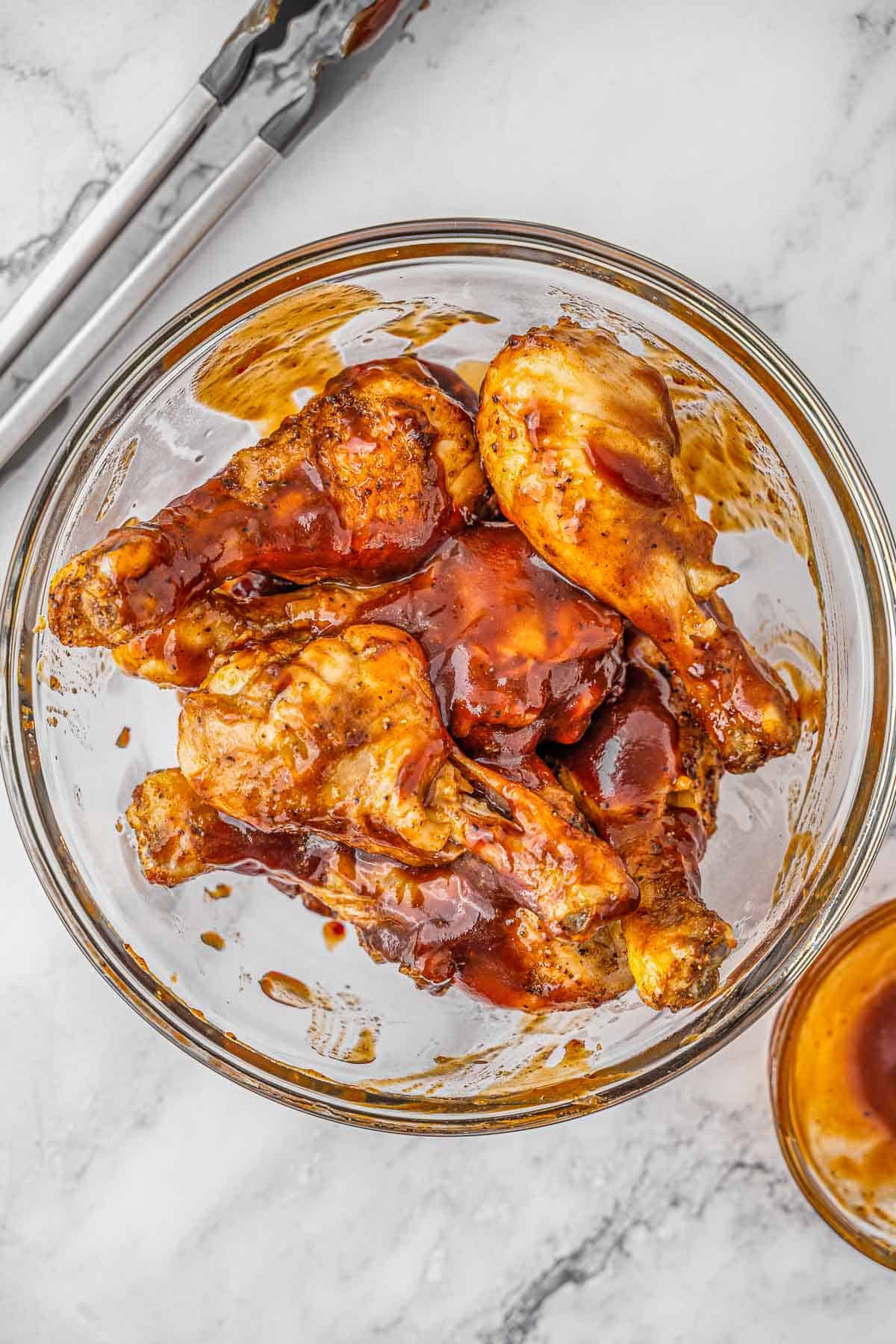 Chicken drumsticks tossed in BBQ sauce in glass bowl.