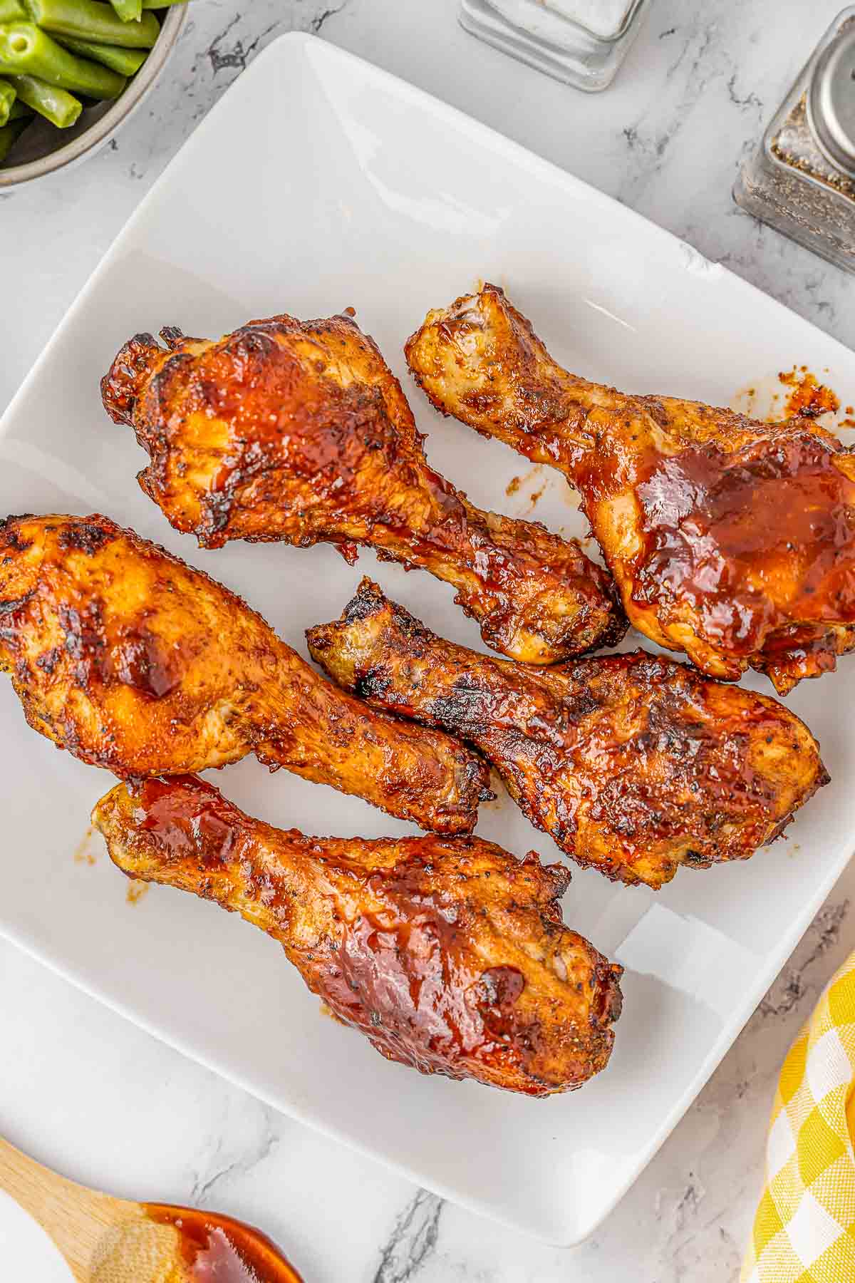 Multiple BBQ chicken drumsticks on a white plate.