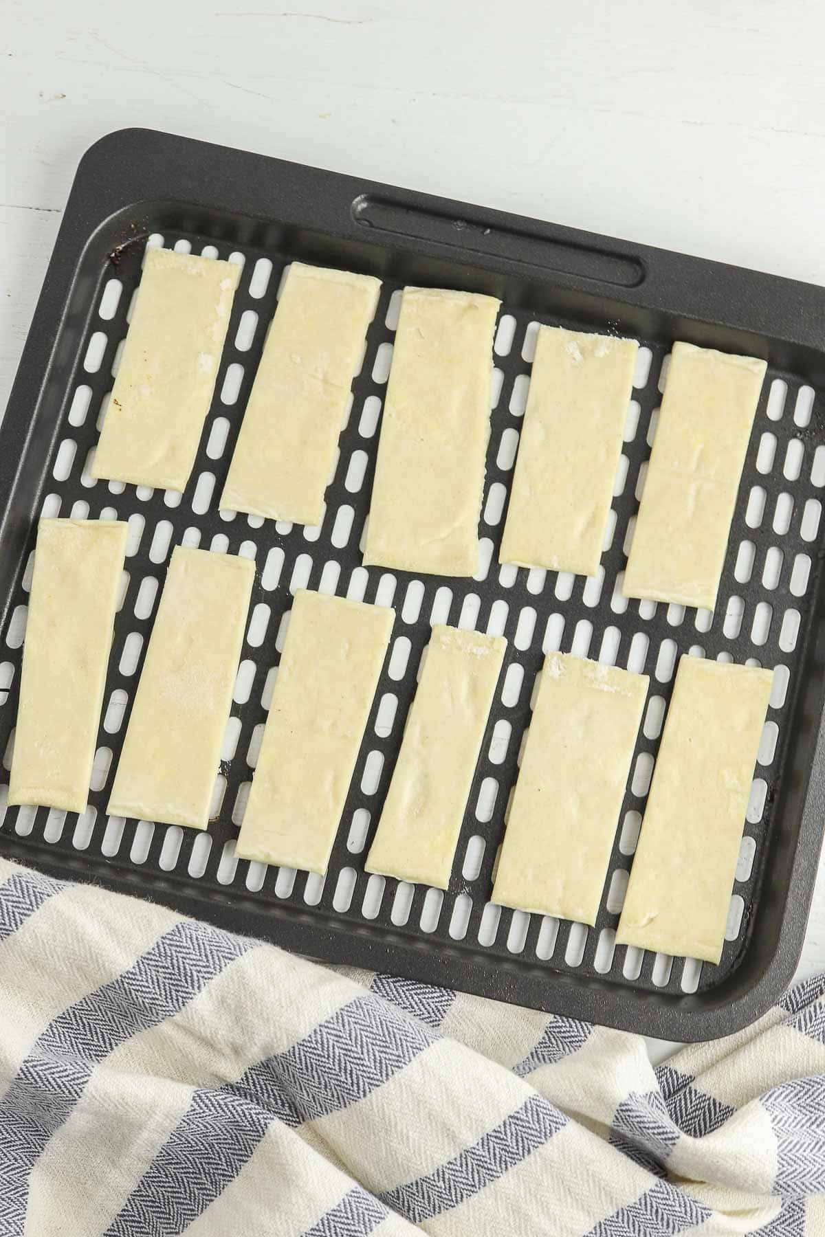eleven strips of puff pastry dough in a black air fryer basket.