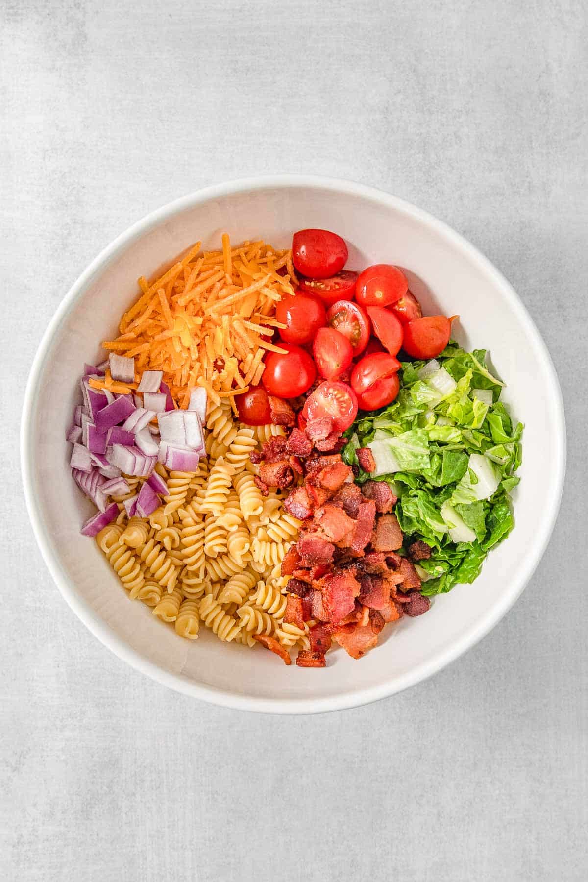 Pasta salad ingredients added to large white mixing bowl.
