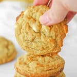 A stack of banana pudding cookies with white chocolate chips with one being held over the stack.