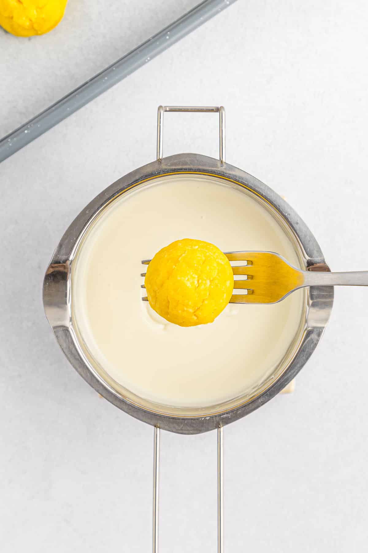 Lemon cake ball on a fork being dipped in frosting.
