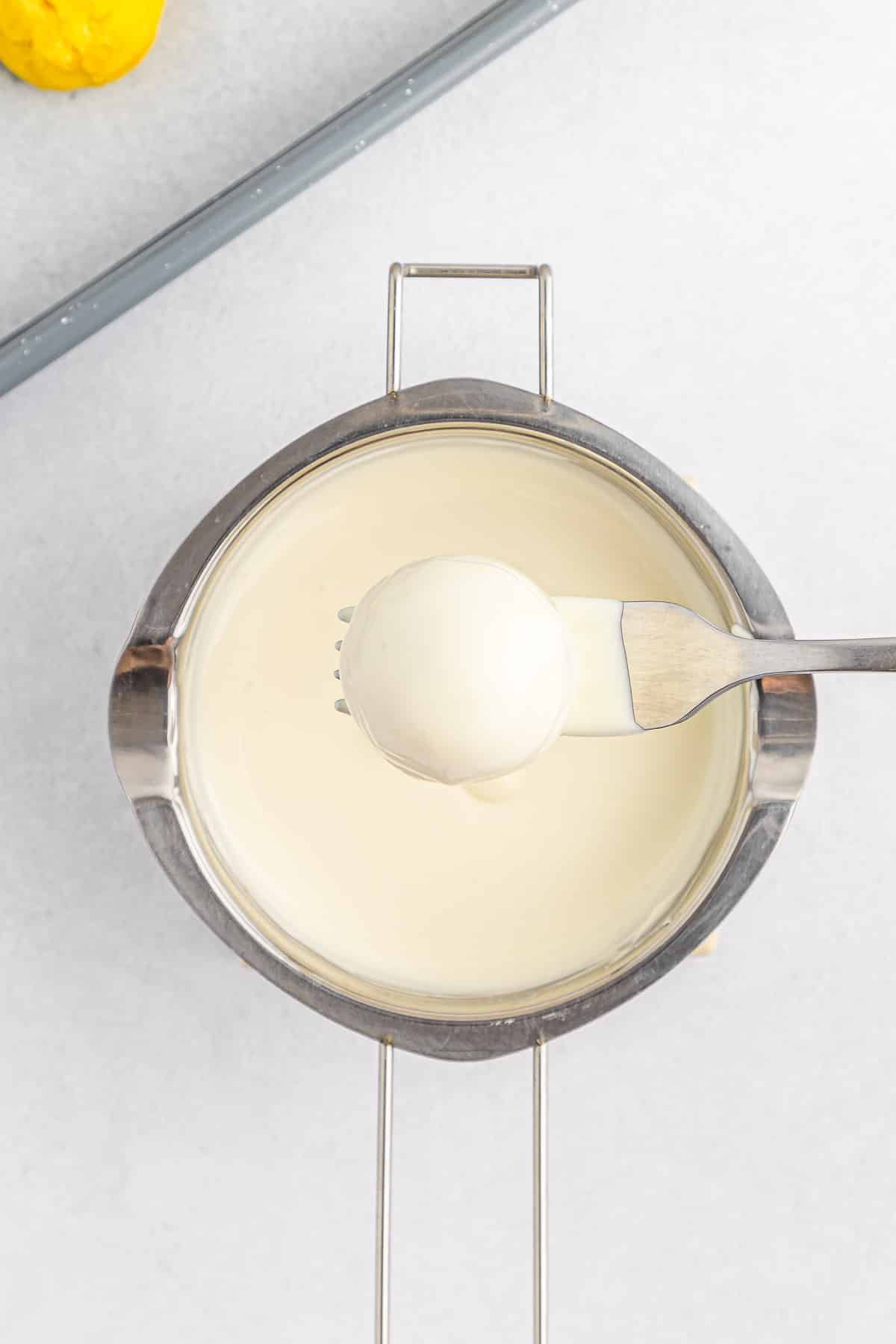 Lemon cake ball on fork being dipped into glaze.