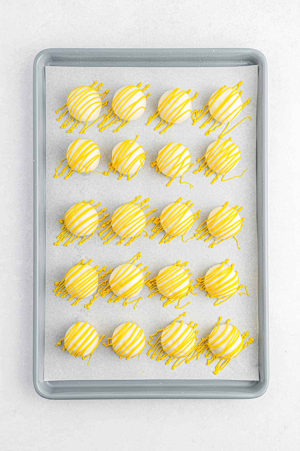 Lemon cake balls with yellow candy drizzle over top on a baking pan.