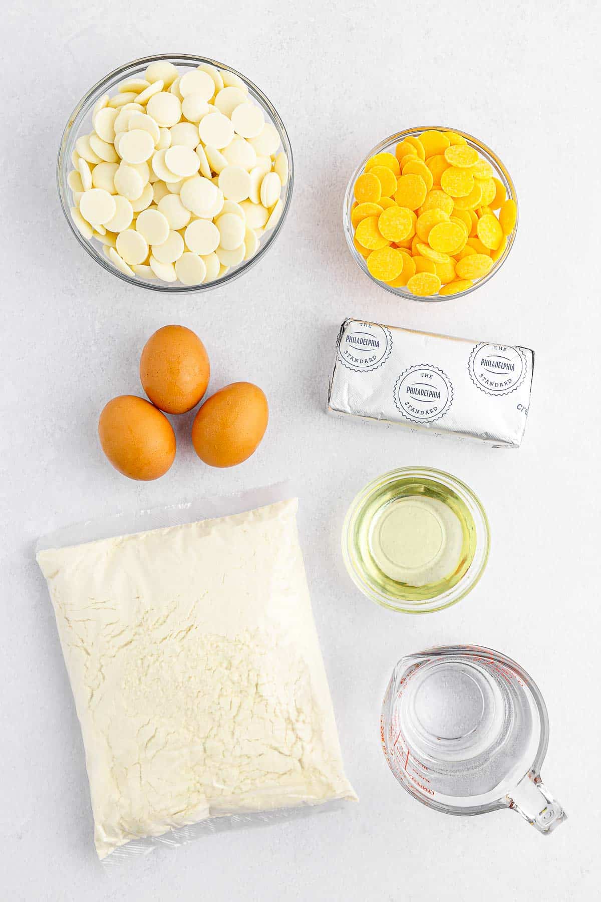 several ingredients for lemon cake balls - cake mix, lemon, cream cheese, eggs, water, vegetable oil and yellow candy melts and vanilla melting wafers.