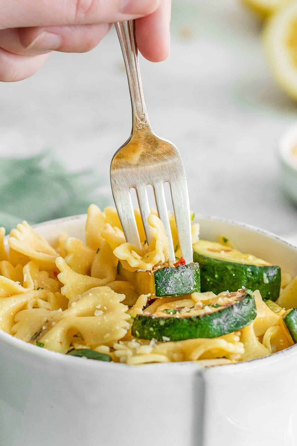 Womens hand holding stick fork into lemon zucchini pasta.