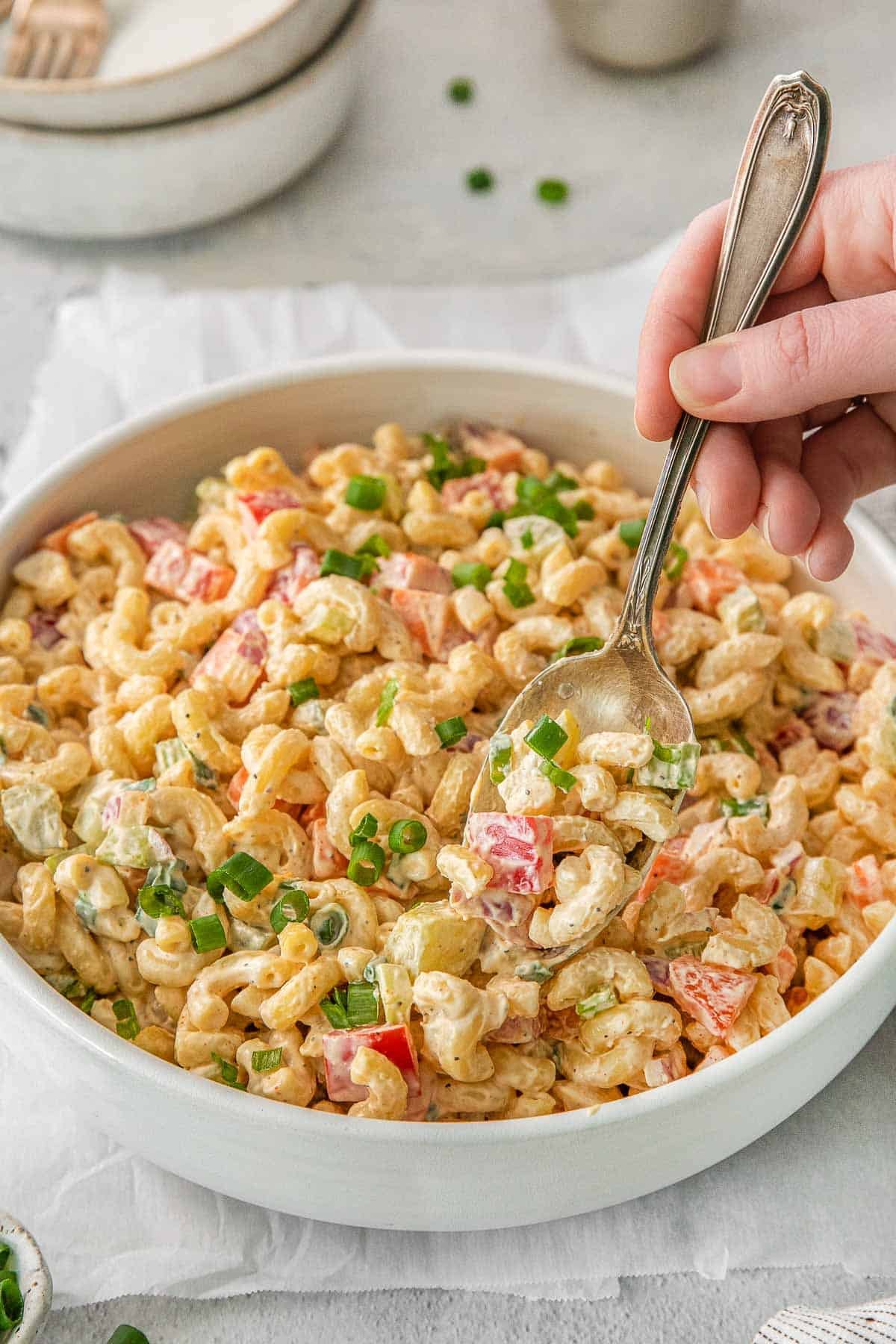 Macaroni Salad in white bowl with women holding spoon.