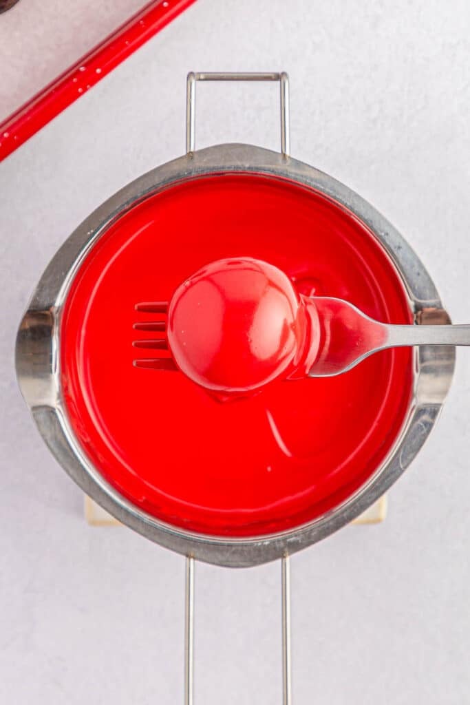 Red oreo ball being dipped into red candy melt.