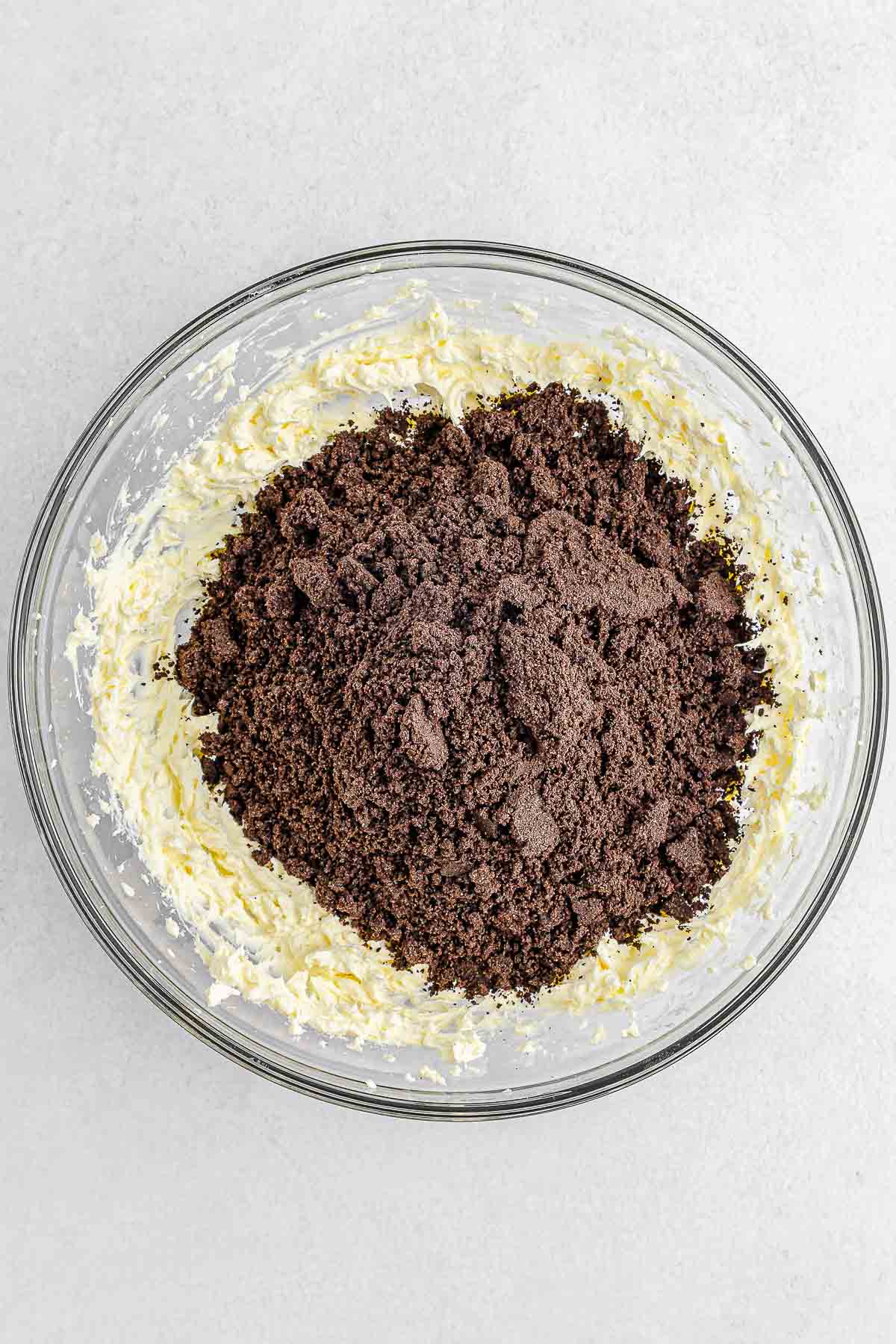 Crumpled oreo added to cream cheese in large glass mixing bowl.