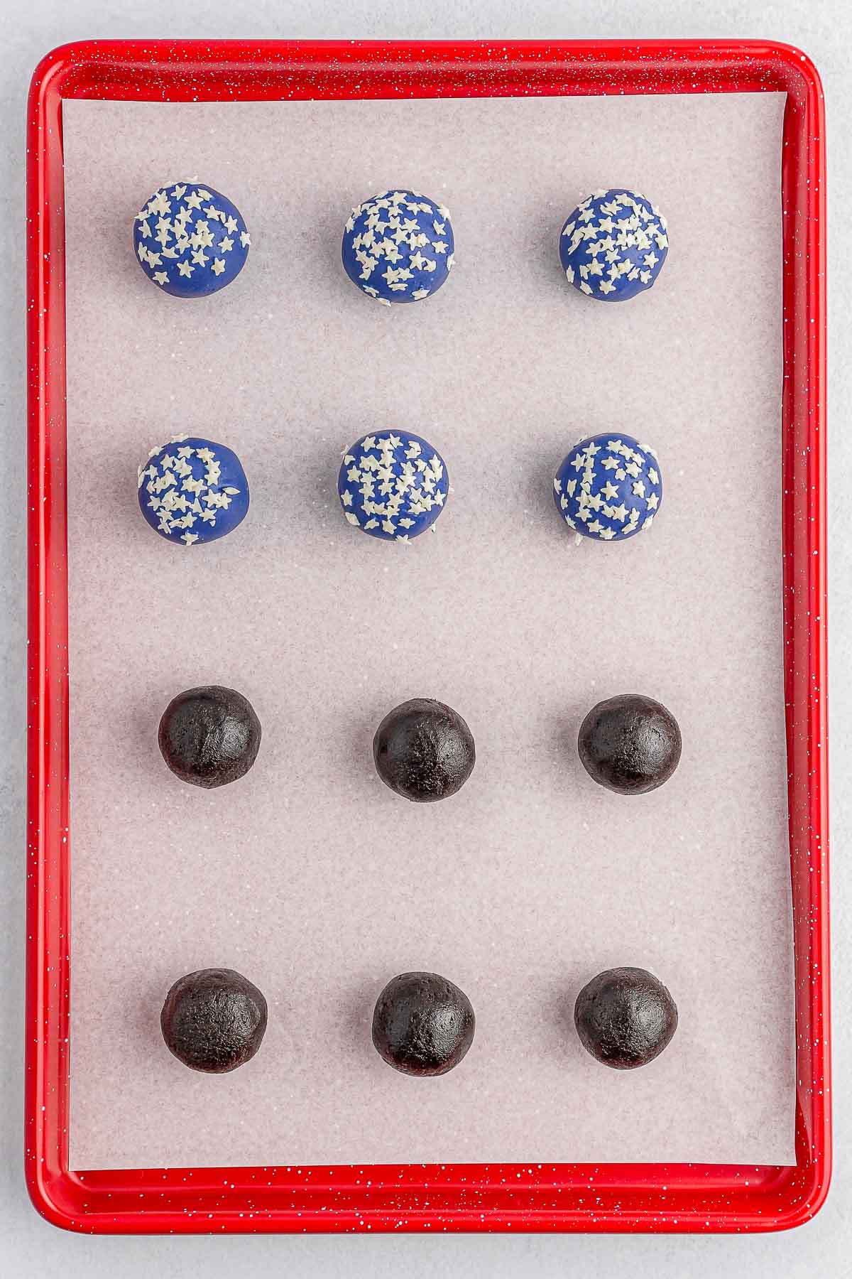 Several blue dipped oreo balls on a red baking sheet.