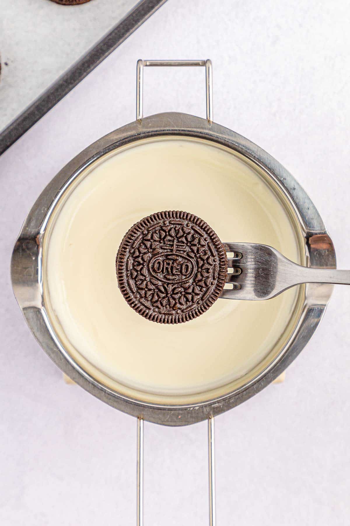 Oreo on a silver fork being held over white candy melt.