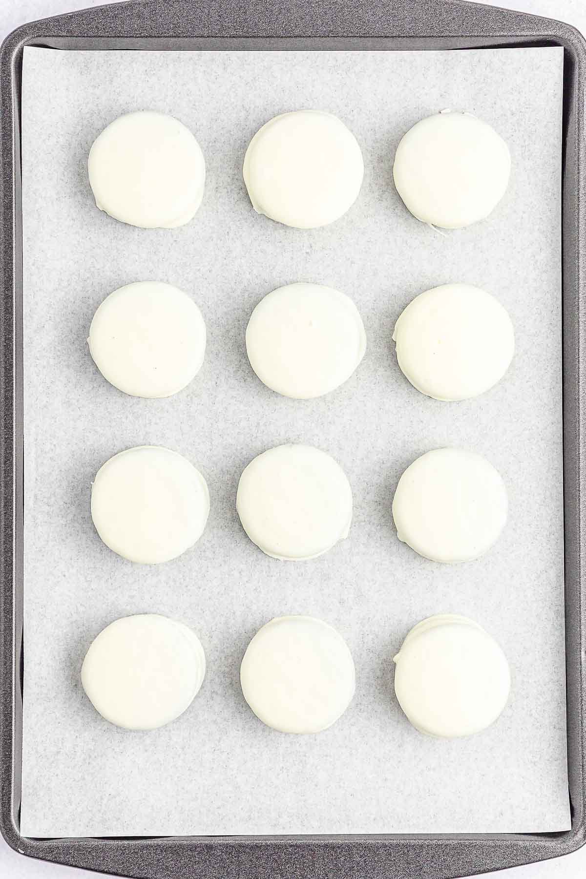 Multiple white coated oreos on a baking sheet.