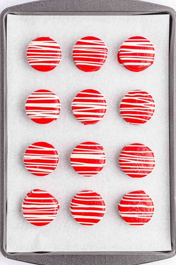 Multiple red patriotic oreos with white drizzle on a baking sheet.