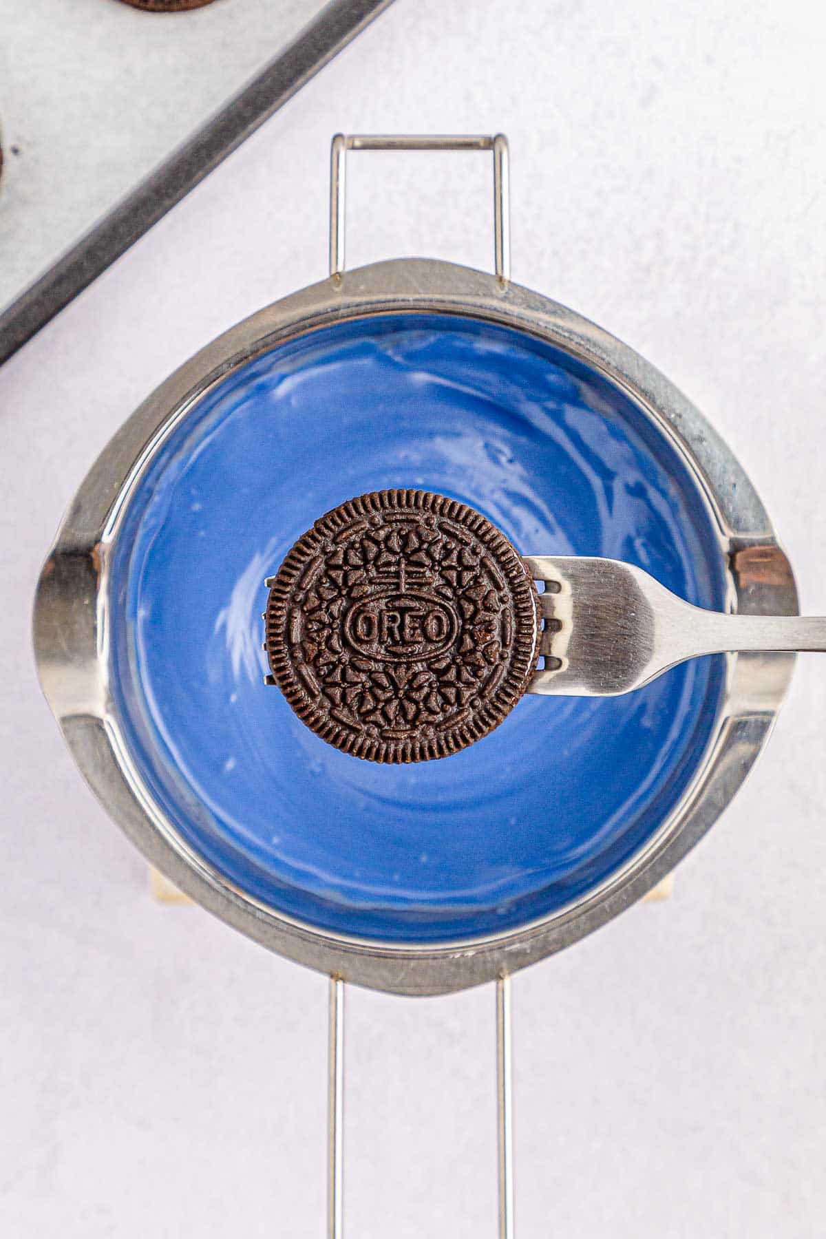 Oreo on fork being held over blue candy melt.