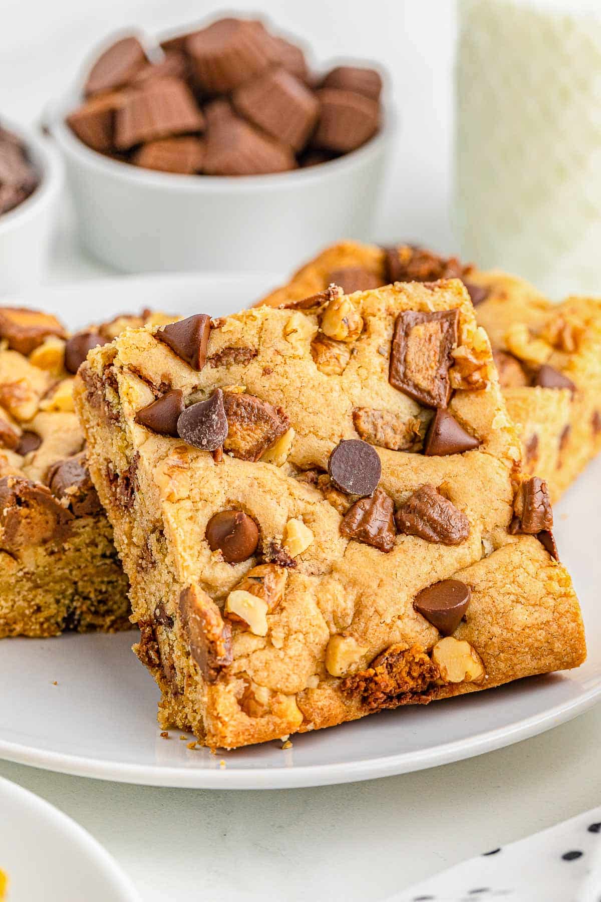 three peanut butter cup cookie bars stacked on a white plate.