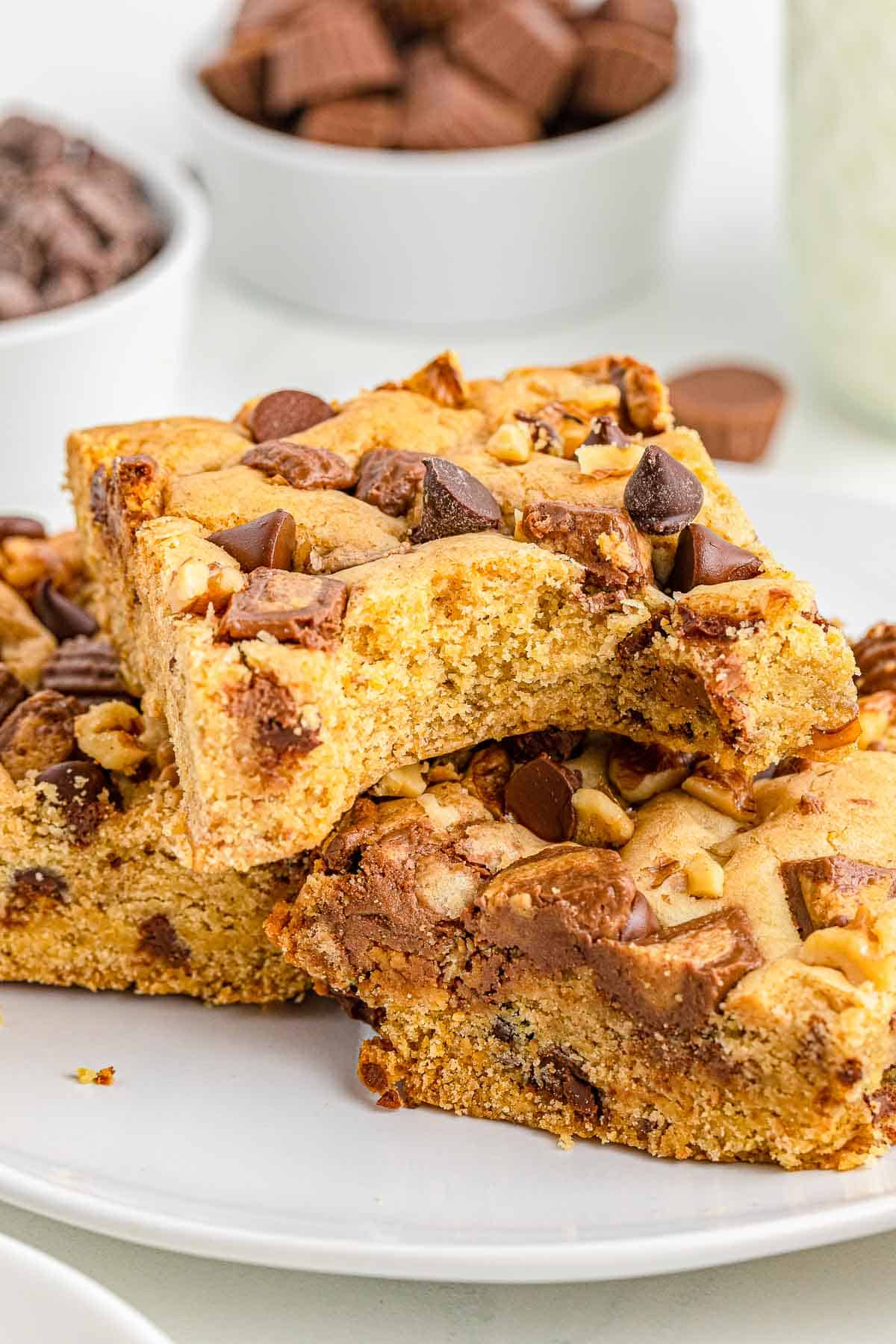 three peanut butter cup cookie bars stacked on a white plate with a bite taken out of the top one.