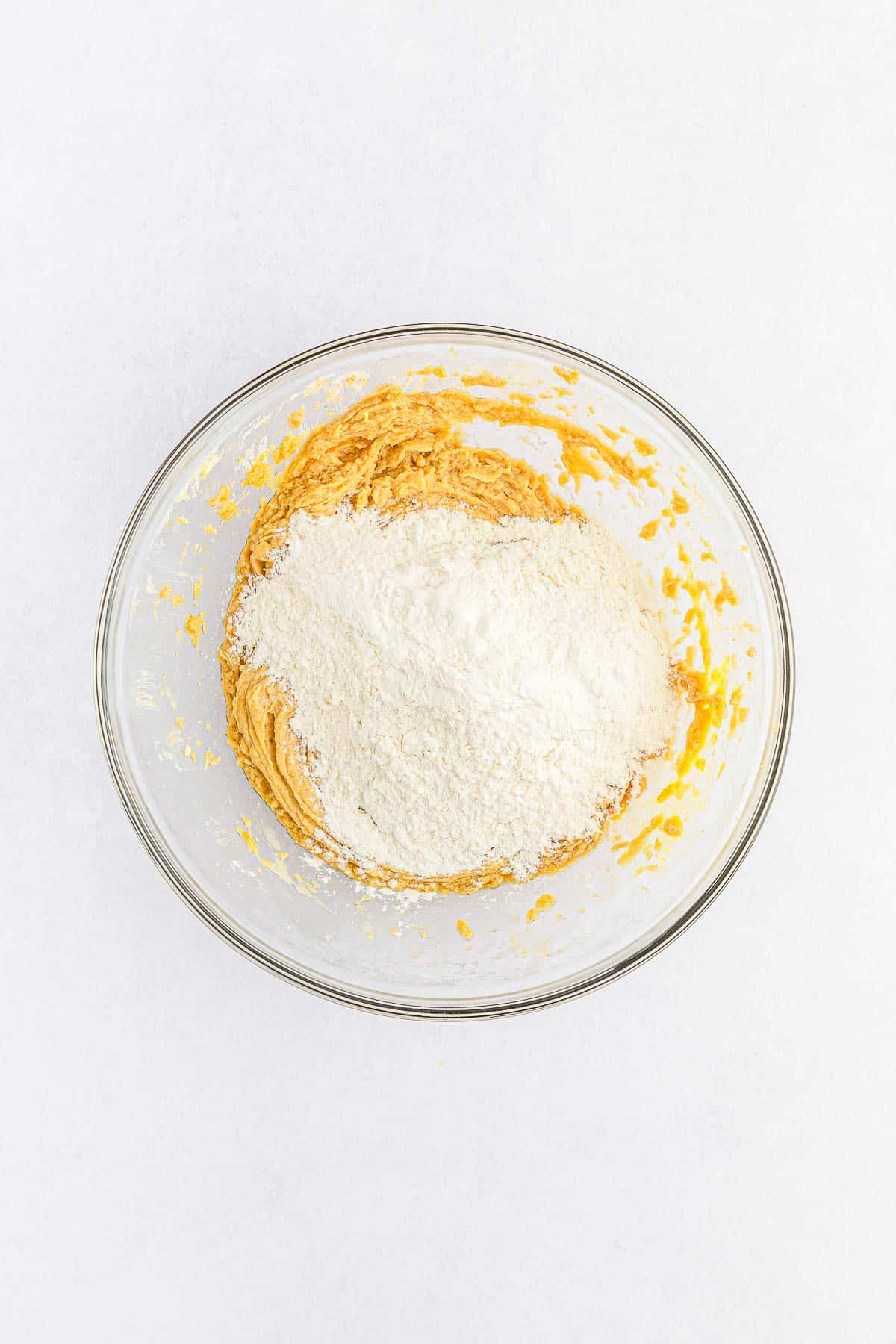 glass mixing bowl with flour on top of sugar and butter mixture.