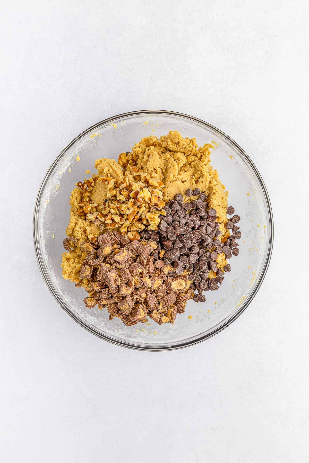 cookie dough with chopped peanut butter cups, chocolate chips and walnuts in a glass mixing bowl.