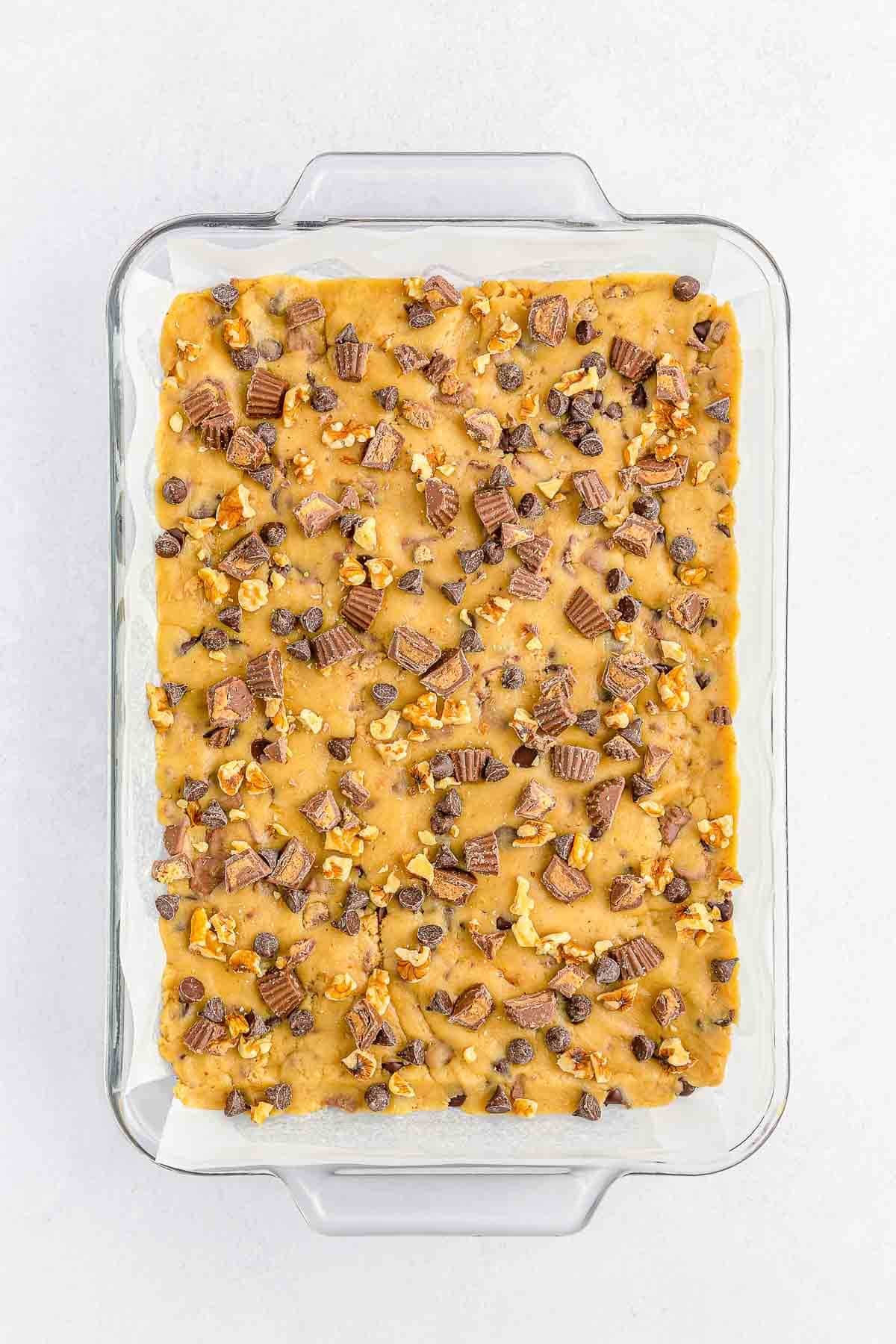 rectangle glass baking dish with cookie bar dough topped with peanut butter cups and chocolate chips.