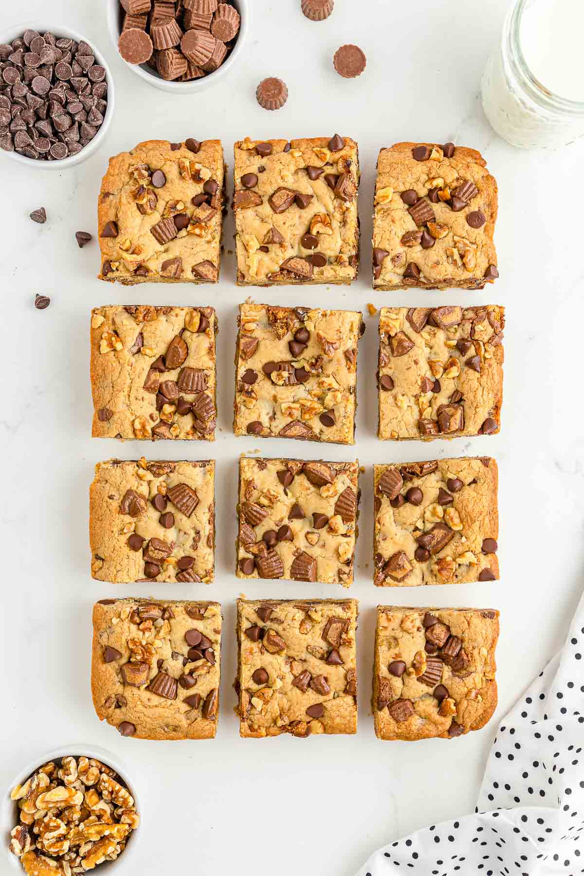 twelve squares of peanut butter cup cookie bars on a counter with a glass of milk.