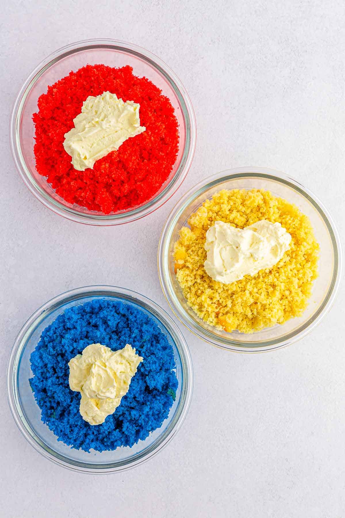 three bowls of crumbled cake batter with cream cheese on top. one blue, one red and one white.