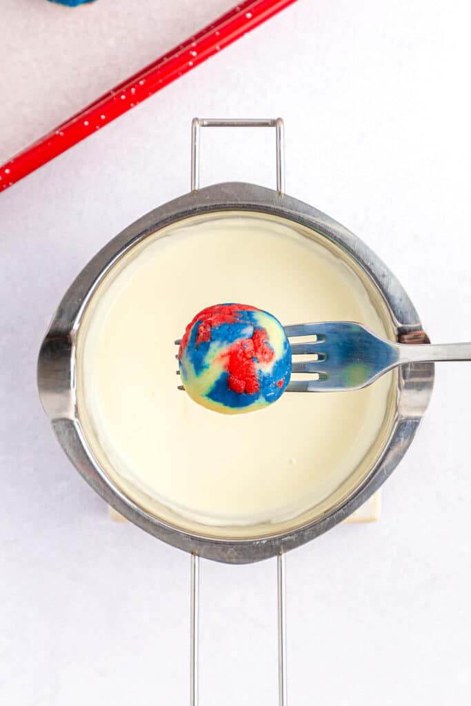 red white and blue cake ball being held over white melted candy wafers.