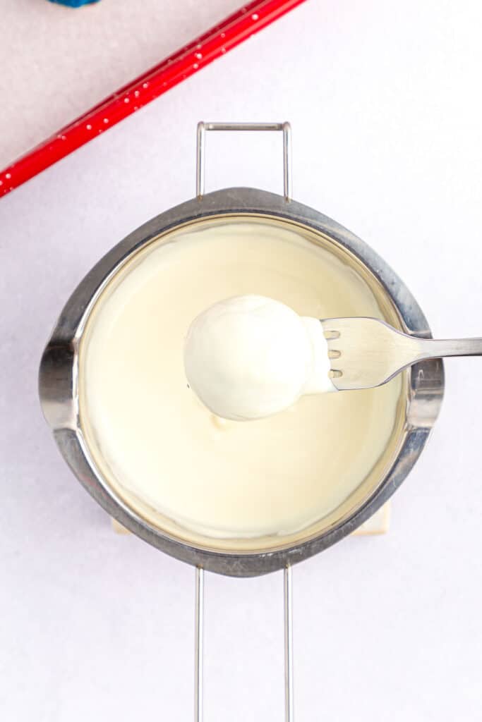 cake ball being dipped into white melted candy 