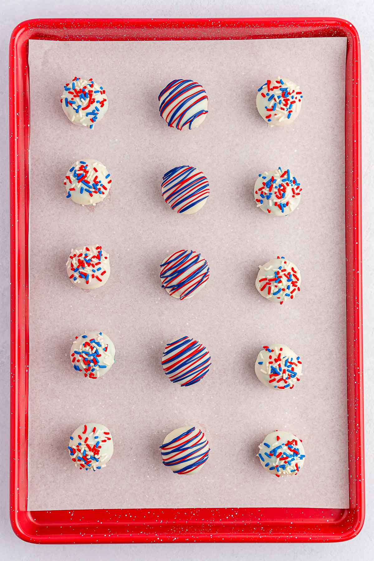 baking sheet with white coated cake balls. come with red white and blue sprinkles and some with red and blue drizzled icing.
