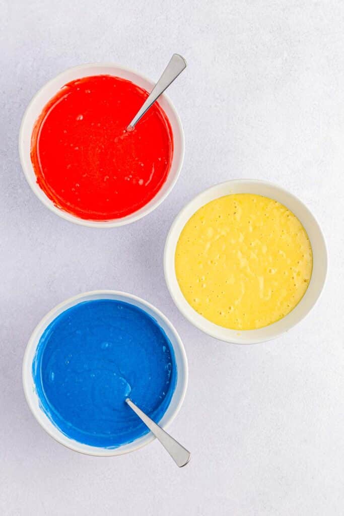 three small bowls of cake batter. one red, one blue and one white.