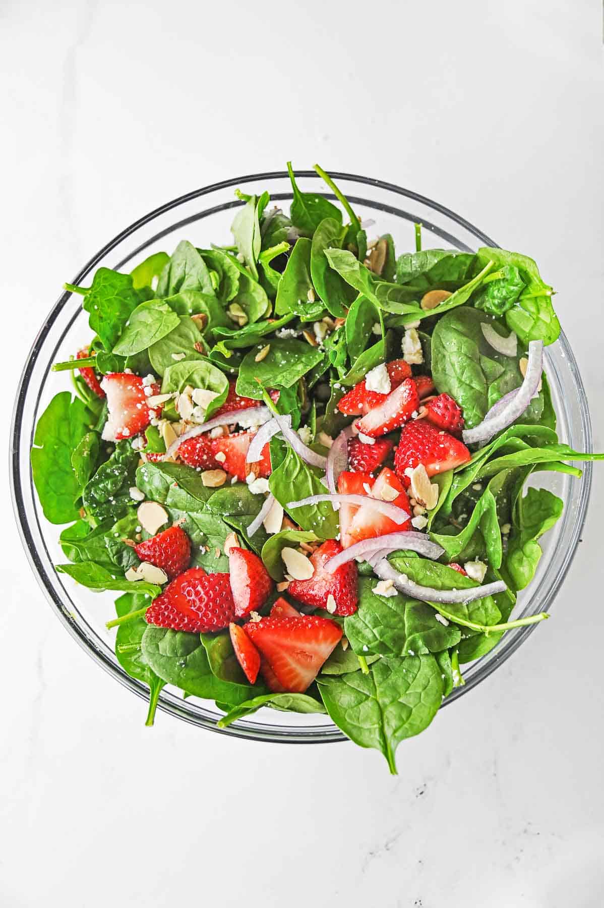 Large glass bowl of strawberry spinach salad ingredients mixed together.