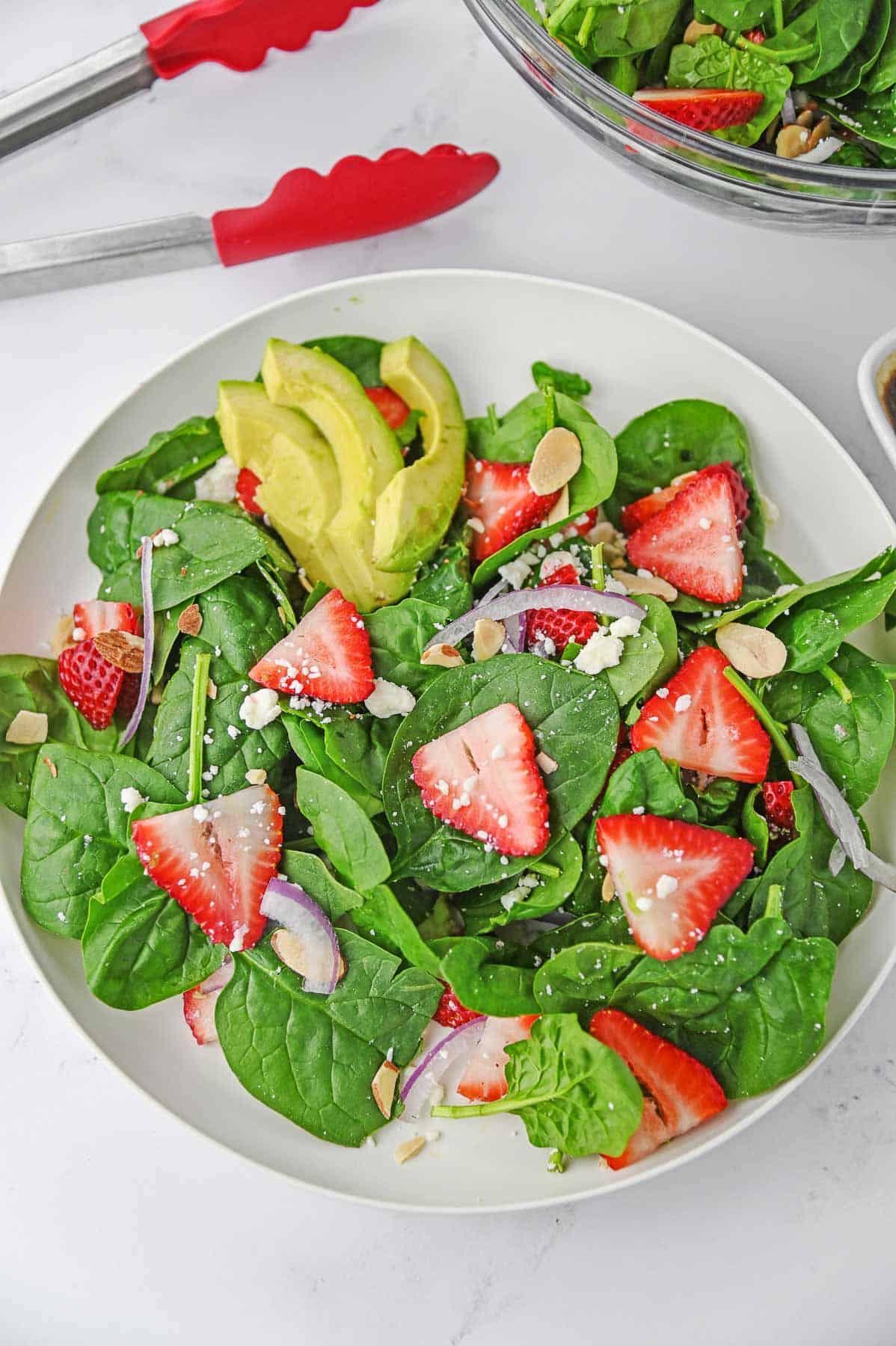 Strawberry spinach salad topped with avocado in a white bowl.