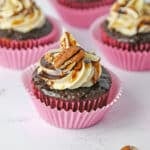 Turtle Cupcake topped with pecans, chocolate and caramel sauce in a pink cupcake liner.