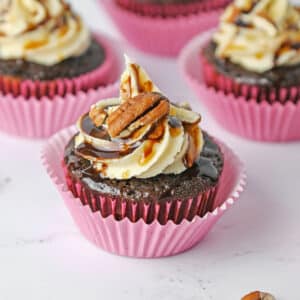 Turtle Cupcake topped with pecans, chocolate and caramel sauce in a pink cupcake liner.