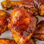 Close up of BBQ chicken drumsticks on white plate.